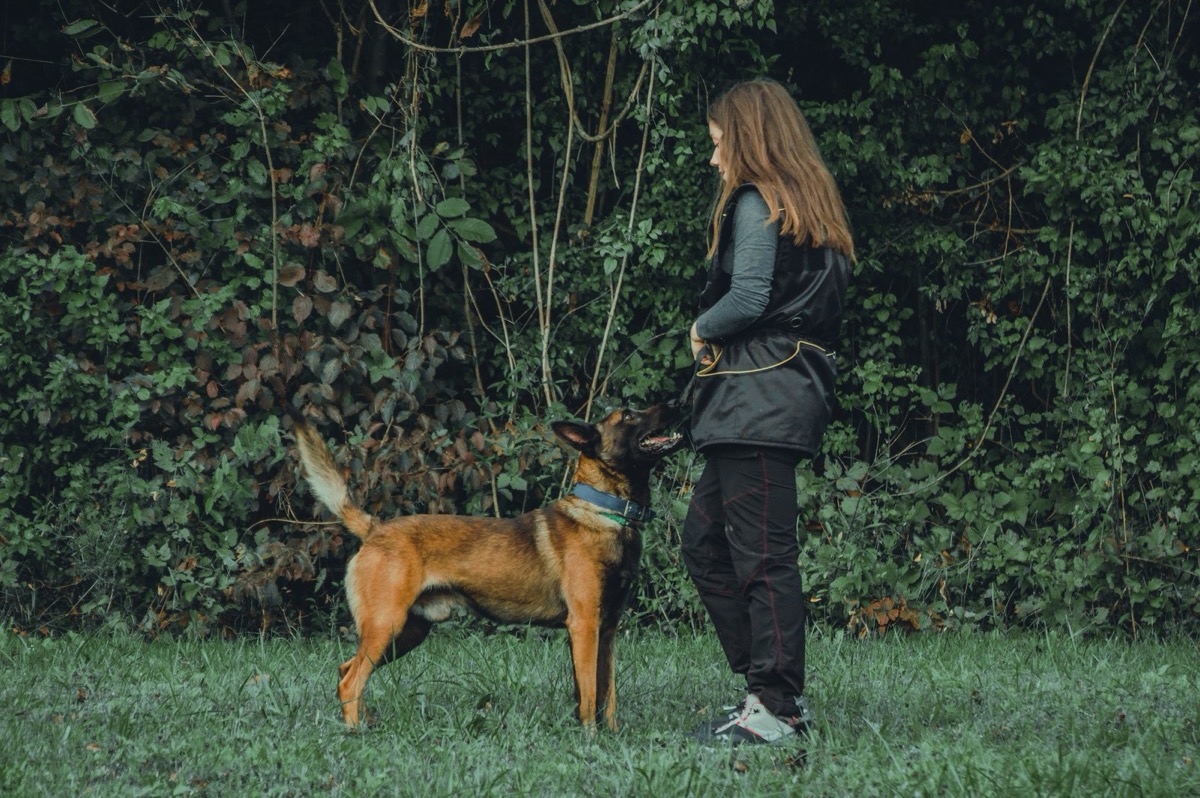 Kvinne står på en gressplen sammen med hunden sin